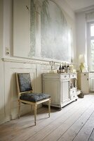 High-ceilinged period room with antique furniture on simple wooden floorboards