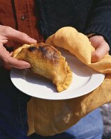 Hände halten Teller mit Empanada