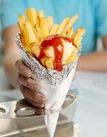 Hand holding a cone of chips with ketchup and mayonnaise