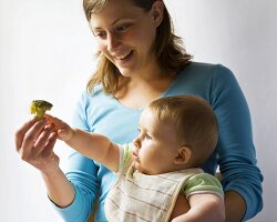 Mother giving baby a broccoli floret