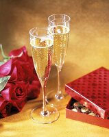 Two Flutes of Champagne, Roses and Candy on Gold Background