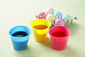 Drei Becher mit Eierfarben, gefärbte Eier im Eierkarton