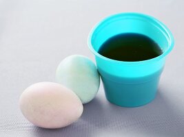 Gefärbte Eier neben Becher mit Eierfarbe