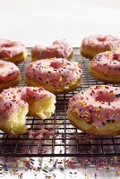 Pink Frosted Doughnuts with Sprinkles on a Cooling Rack; One Bitten