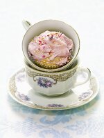 A cupcake with pink cream and sugar balls in a cup