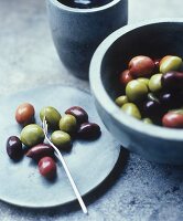 Grüne, rote und schwarze Oliven auf Teller und in Schüssel