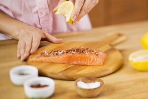 Woman Squeezing a Lemon Wedge over Salmon