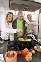 Mann und zwei Frauen kochen gemeinsam ein Wokgericht