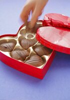 Hand taking chocolate out of heart-shaped box