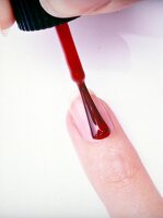 Close-up of red nail paint being applied on woman's nail