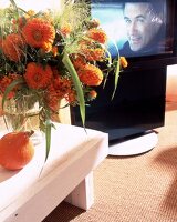 Drehbares TV-Set hinter orangem Blumenstrauss
