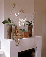Drei blühende Orchideen stehen in Metalltöpfen auf dem Kamin