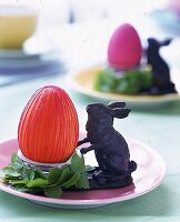 Deko-Ei im Eierbecher, daneben kleiner Hase aus Metall