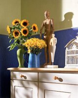 Blumenvasen sind neben Holzstatuen auf d. Kommode dekor.(Sonnenblumen)