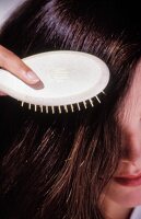 Dunkelhaarige Frau bürstet ihre Haare mit einer Bürste aus Holz
