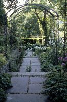 Natursteinweg von Rosenbögen überspannt führt in den Garten