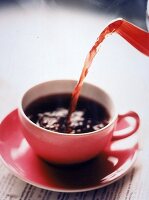 Aus einer Kanne wird Kaffee in eine Tasse eingeschenkt