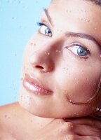 Close-up of beautiful blue eyed woman leaning on glass with water droplets