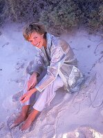 Frau sitzt im Sand, blaue Workerhose transparenter Nylon Parka