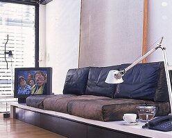 Ledersofa,dahinter ein laufender Fernseher