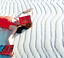 Frau liegt im Sand, ein Buch auf dem weGesicht, ein Buch in jeder Hand