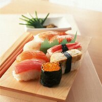 Mehrere Nigiri-Sushi auf einem Holzbrett.X