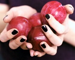 Close-up of woman's hand wearing black nail paint, holding red plums