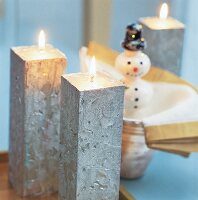 Silberfarbene quadratische Kerzen brennen neben einer Schneemannfigur