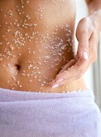 Close-up of woman rubbing sea salt to her belly, mid section