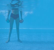 Frau steht im Pool hält unter Wasser zwei Bälle, Rückentraining