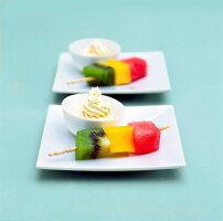 Fruit skewers with kiwi, mango, watermelon and bowl of passion fruit dip on plates