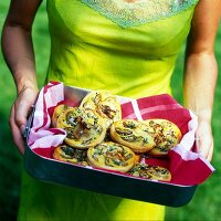 A woman carrying aubergine and potato tartlets in a baking tin