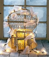 Antique bird cage decorated with pillar candles, fairy lights and white feathers