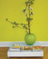 flacher Couchtisch mit Zeitschriften + grüner Vase vor grüner Wand