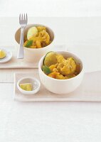 Blumenkohl-Curry mit Kokos in weißen Schälchen, Limettenscheiben, Gabel