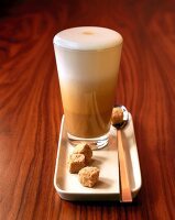 Latte macchiato in glass on white plate with sugar cubes on wooden surface