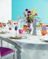 Tisch, dekoriert mit Blumen, bunten Gläsern, Osterei in einem Eierbecher