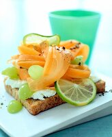 Close-up of toasted bread with cream cheese, grapes, carrots and lime on square plate