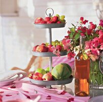 Eine Zinketagere mit Obst auf einer rosa Tischdecke