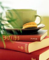 Close-up of green tea cup and biscuits on pile of books