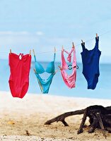 Different coloured swimwear hanging on string at the beach.