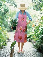 Gardener wearing pink apron and straw hat holding plant pot with parrot