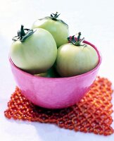 Close-up of green tomatoes in pink bowl on white background