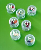 Multi-coloured pills for hormones in small glass boxes on green background 