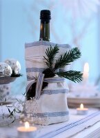 Bottle wrapped with napkin, pine tree leaves and lit tea lights candles on table