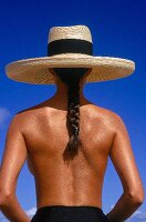 Rear view of semi dressed woman with long plaits wearing sunhat against blue sky