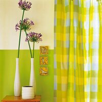 Vases and allium flowers on a stool in front of a green-and-white wall next to green-and-yellow checked curtains