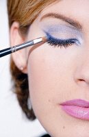 Close-up of woman applying blue eyeliner with brush on the upper eyelid