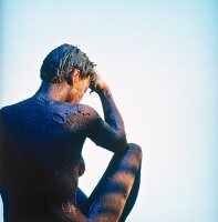 Rear view of nude woman sitting quietly with knees up and body wrapped in sea mud 