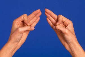 Close-up of woman's hand performing acupressure mudra against blue background